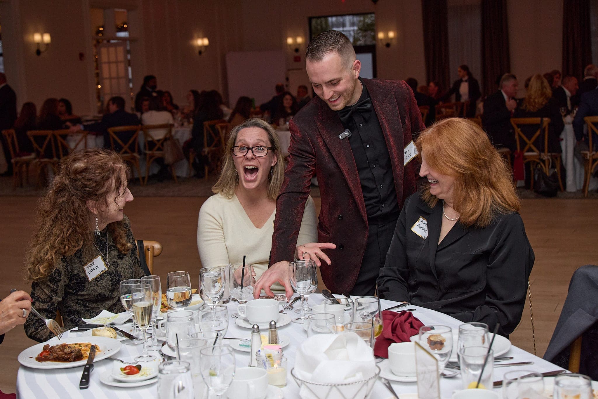 Guest gasping at a dinner table as Chris Dare reveals a card among the place settings