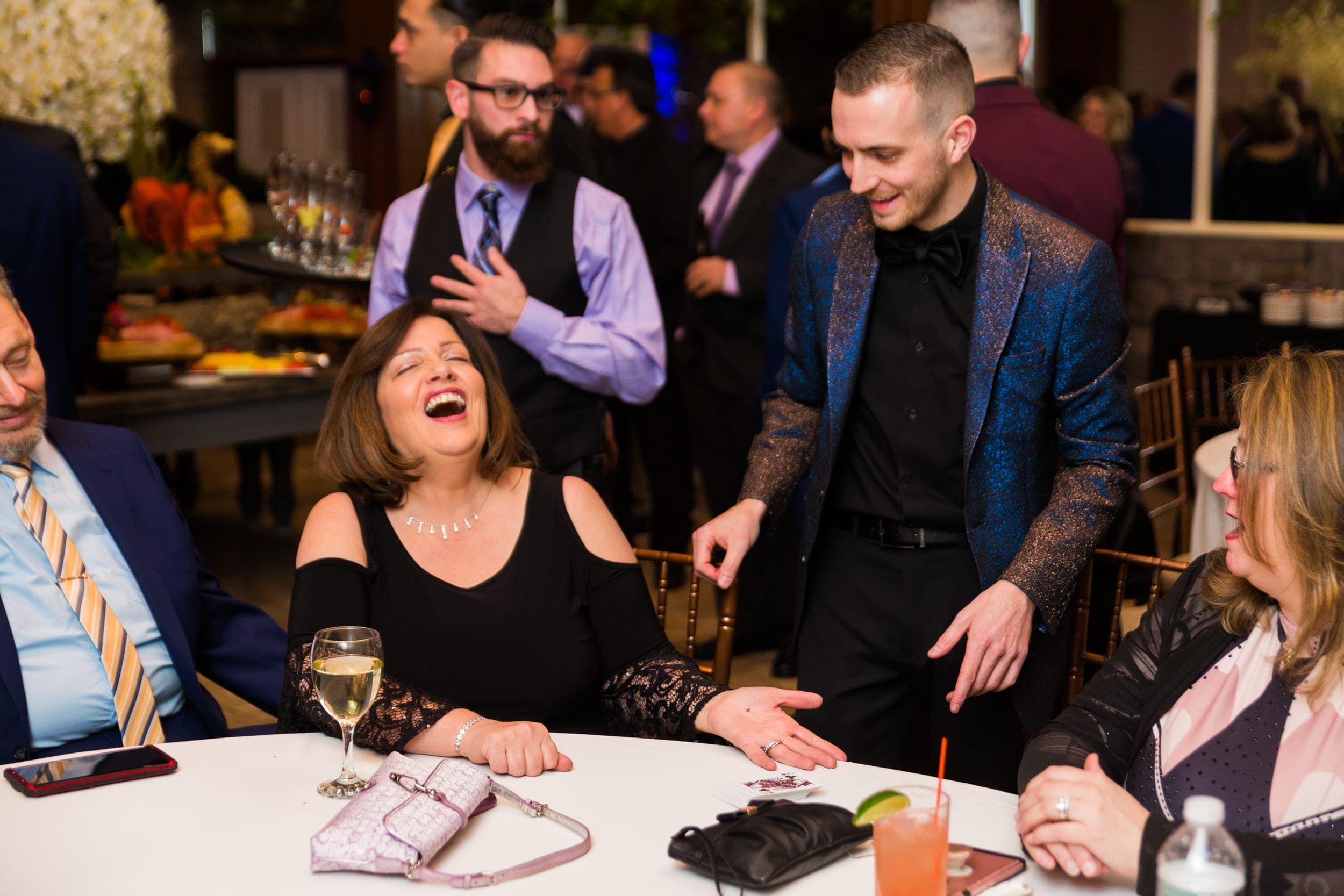 Guest laughing as her chosen card appears beneath her outstretched hand at a cocktail reception