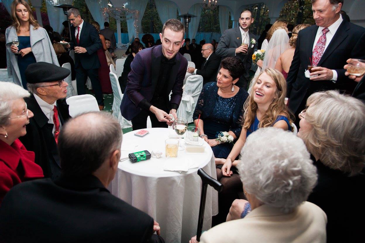 Chris Dare performing table magic for seated guests at a tented reception