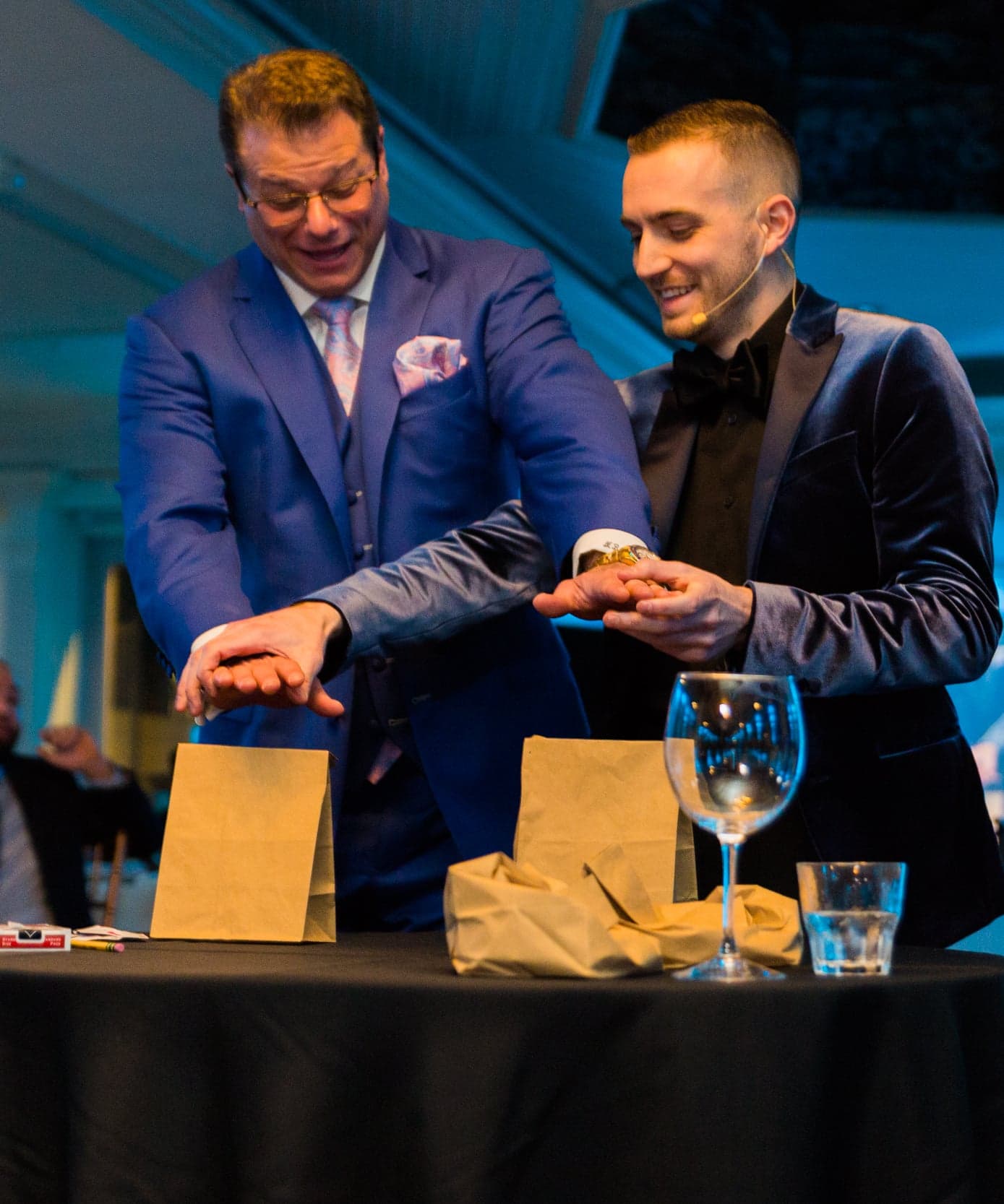 Chris Dare and a volunteer hold their fists over paper bags during an on-stage gamble routine at a corporate gala
