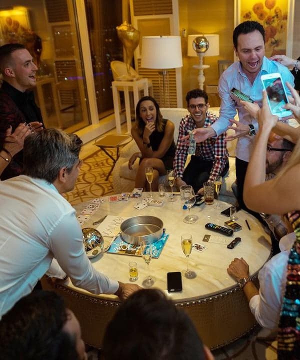 Guests around a marble table in a penthouse suite laugh and film on their phones as Chris Dare performs at a private party